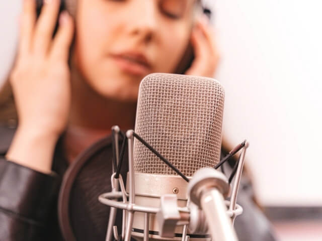 Imagem de uma mulher desfocada ao fundo e um microfone a frente sem desfoque