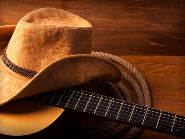 um chapéu e um violão em cima de um fundo de madeira. Representando a música sertaneja no Brasil