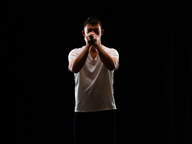 Homem cantando em um fundo escuro com as mãos sobre o microfone