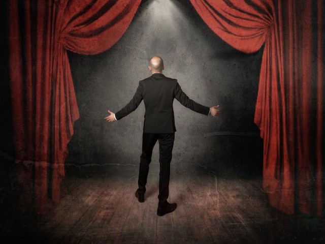 palco de teatro musical um homem jovem, calvo de costas para o público 